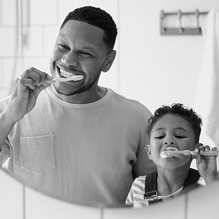 A father and son brush their teeth.