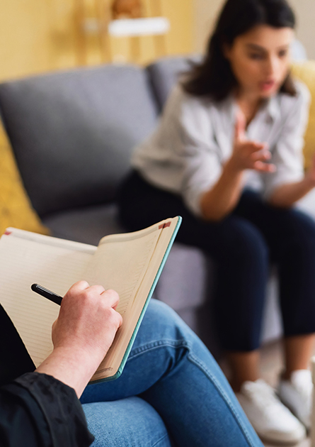 A woman speaks with a therapist as the therapist takes notes