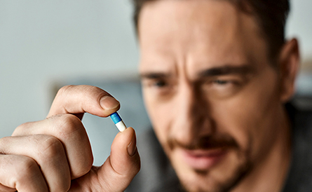 A man looking closely at a pill pinched in between his thumb and index finger