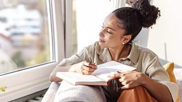 A woman writing in a journal while looking out the window