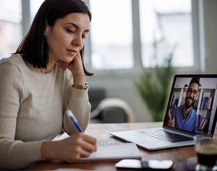 A person takes notes while talking to someone on a video call