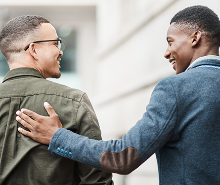 Two men talking and smiling while one rests his hand on the other's back
