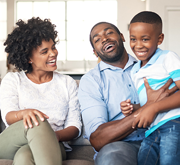 A smiling husband and wife, with a smiling child on the husband's lap