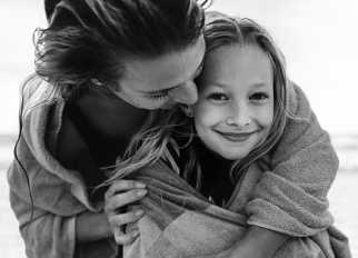 A little girl smiles as her mother holds her 