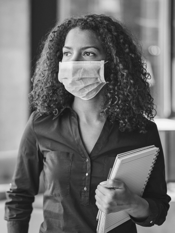 A masked woman looks out her office building's window