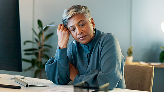 A woman closes her eyes and rests her head in her hand.