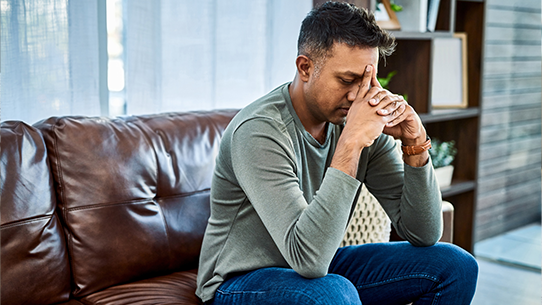 A man sits and rests his hands on his head. 