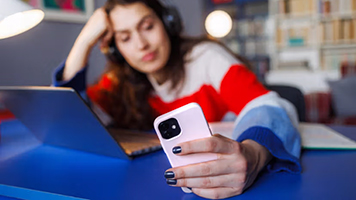 A person sits in front of their laptop looking at their phone