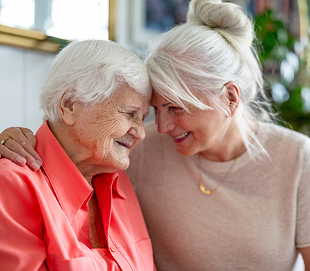 An older woman and a younger woman embrace with their foreheads touching.