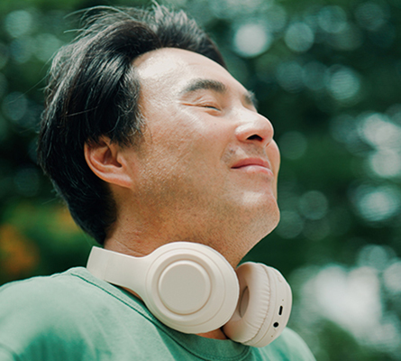 A young man wearing headphones stands outside and takes a deep breath.