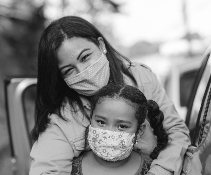 A mother and daughter smile together under masks