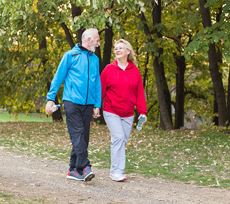 A smiling elderly couple holding hands while walking through a park