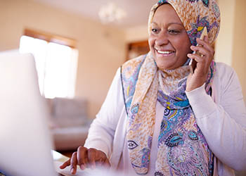 A smiling elderly woman talking on her phone while looking at a laptop