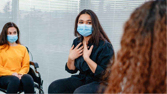 Women in masks sit and discuss mental health