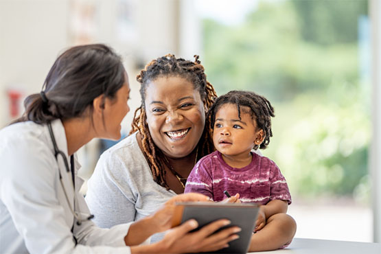 A mother with young child laughs with a healthcare provider