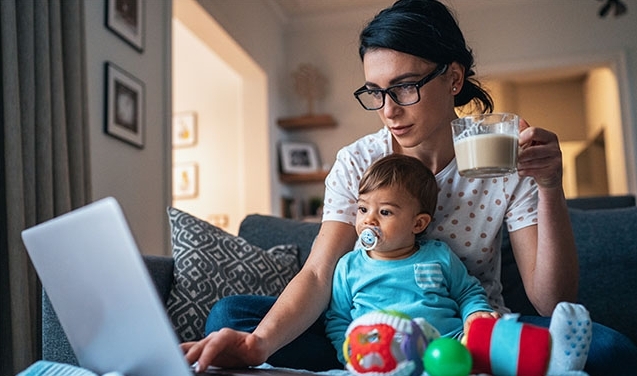 young mother with baby in lap looks at laptop
