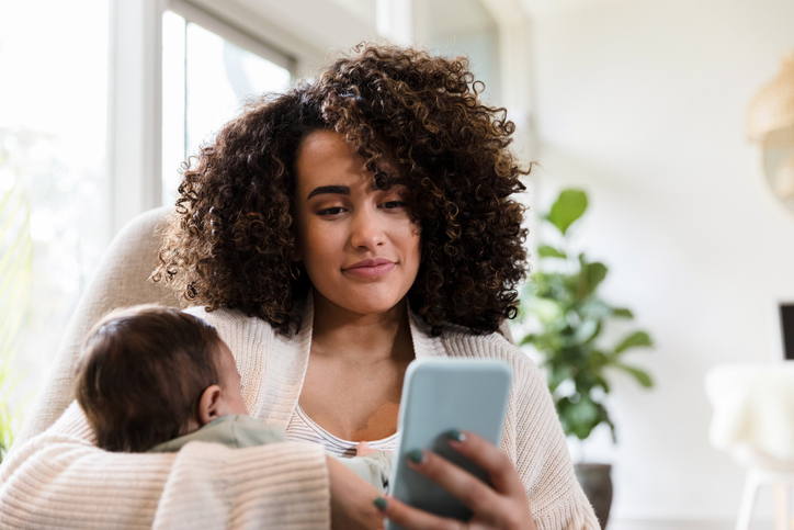 A mother holds her baby while looking at her phone