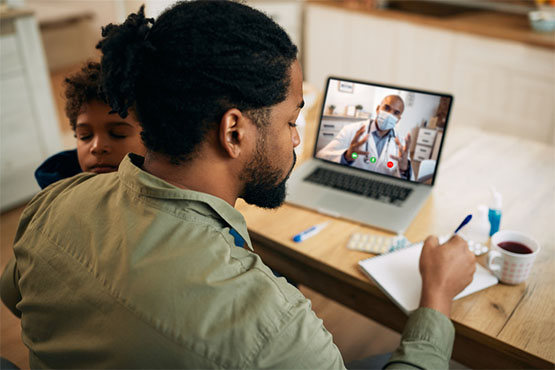 A patient takes notes from his telehealth care provider; a child sleeps in his lap
