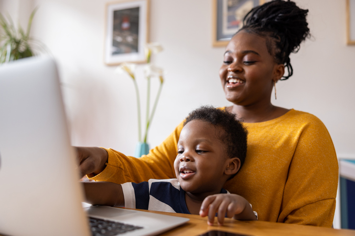 A mother uses the computer with her young son
