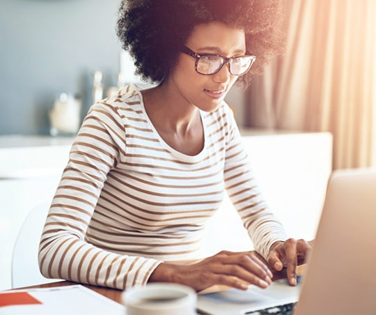 A woman sits at a desk typing on her laptop