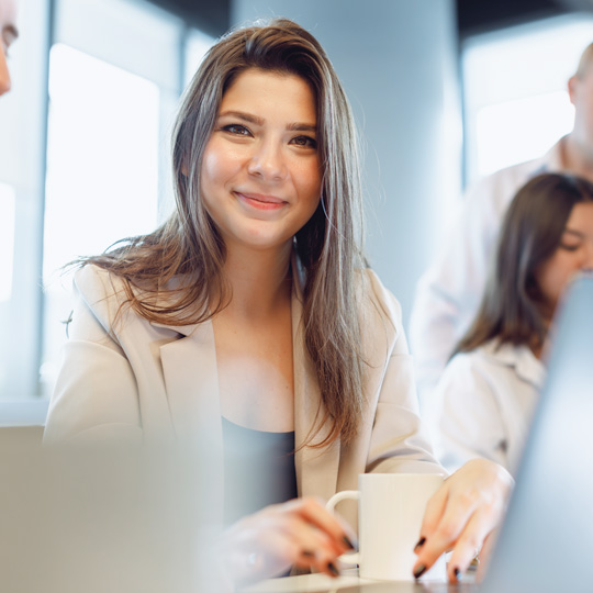 A woman smiles while holding a cup of coffee