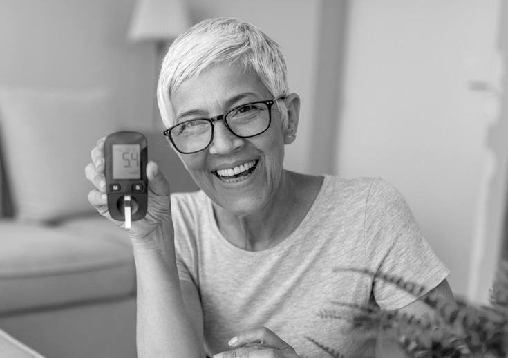 A woman smiles as she holds up a blood glucose meter