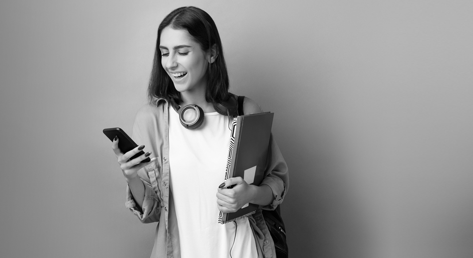 A young woman smiles while looking at her mobile device.