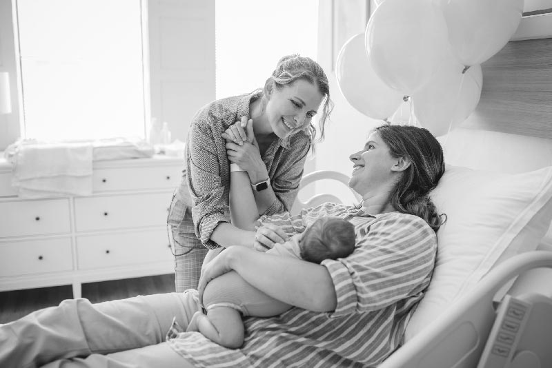 A woman holds her friend's hand as she holds a newborn baby. 
