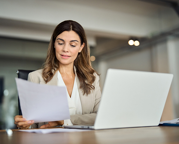 A woman at a conference table looks at paperwork while sitting in front of her laptop.