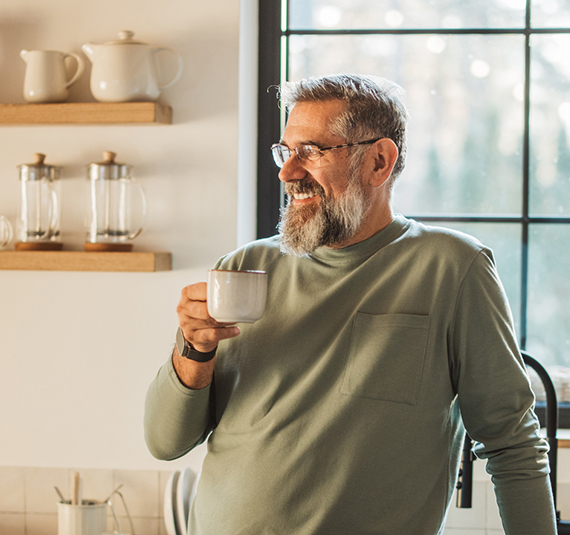 A man stands with a cup of coffee in his kitchen