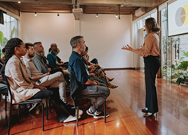 A woman gives a presentation in front of a seated group of people.
