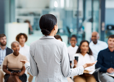 A woman gives a speech standing in front of a group of people 