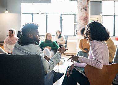 A man and a woman talk while seated next to each other at a workshop.