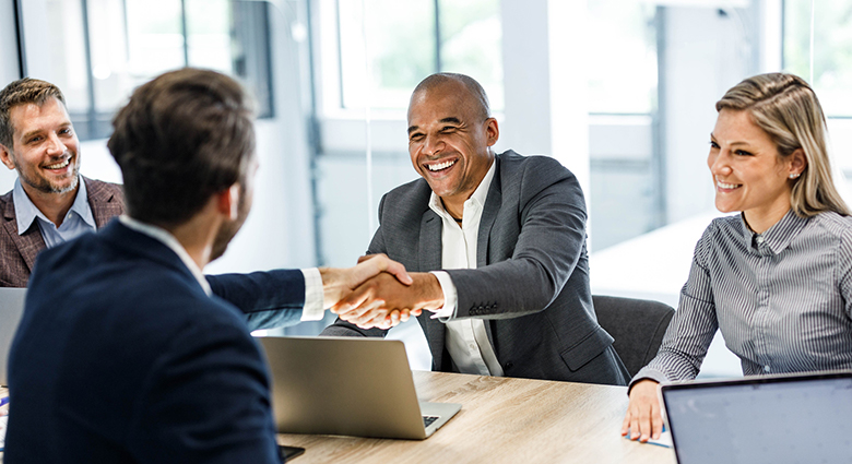 Two men shakes hands over a conference table during a business meeting.