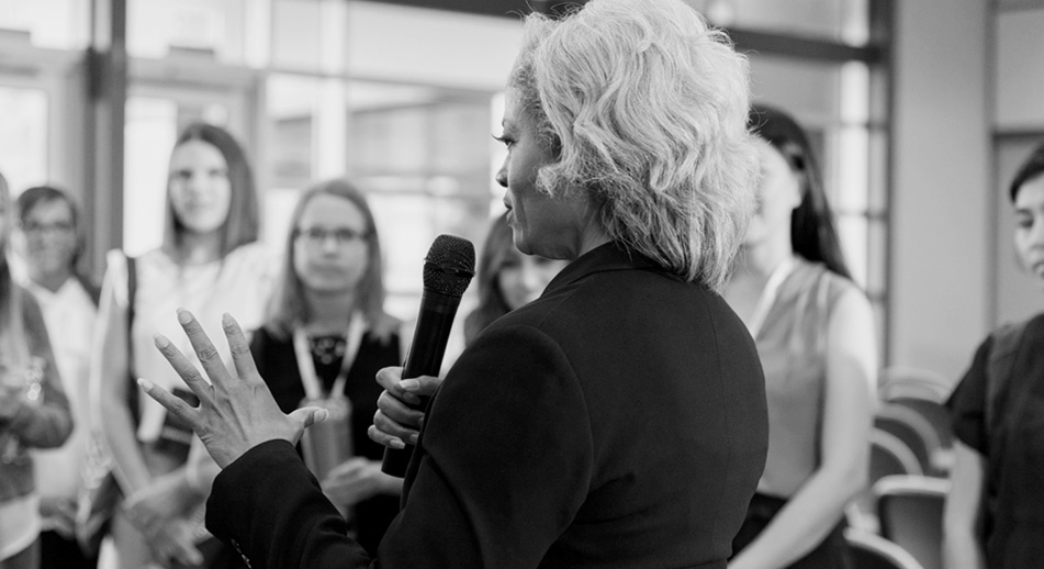 A woman holds a microphone while talking with a group of people. 