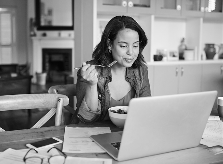 A woman at a laptop eating breakfast