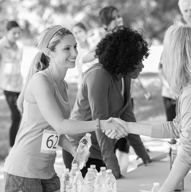 A woman runner holds a water bottle and shakes hands with another woman.