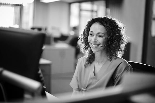 A nurse smiles while talking to someone on a headset.