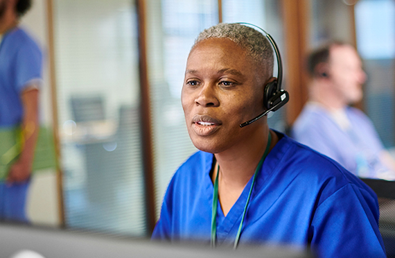 A nurse smiles while talking to someone on a headset.