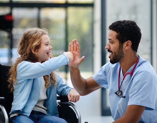 A girl using a wheelchair fistbumps a doctor who kneels by her side.