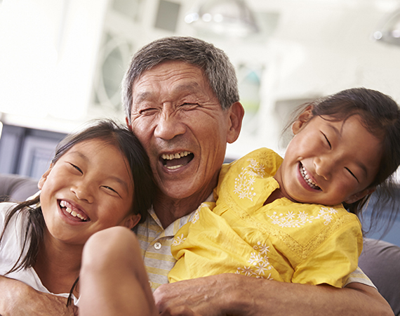 A grandfather and his two granddaughters laugh while embracing each other.