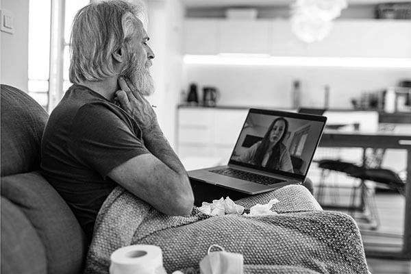 A sick man sits on the couch having a virtual care visit