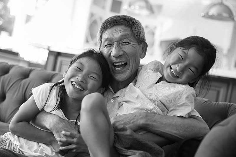 A grandfather and his two granddaughters laugh while embracing.