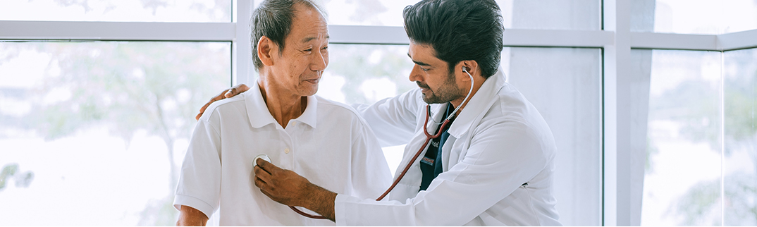 An older man has his heart rate checked by a doctor with a stethoscope.