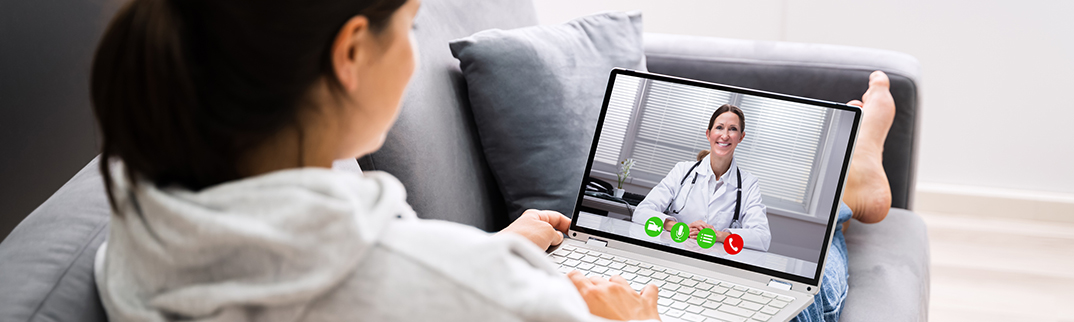 A woman sits on a couch with her computer while having a virtual visit.