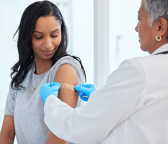 A doctor places a small bandage on a woman's upper arm.