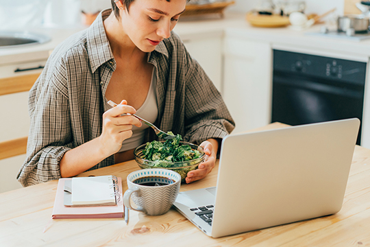 A woman reads about her plan online while eating a salad.