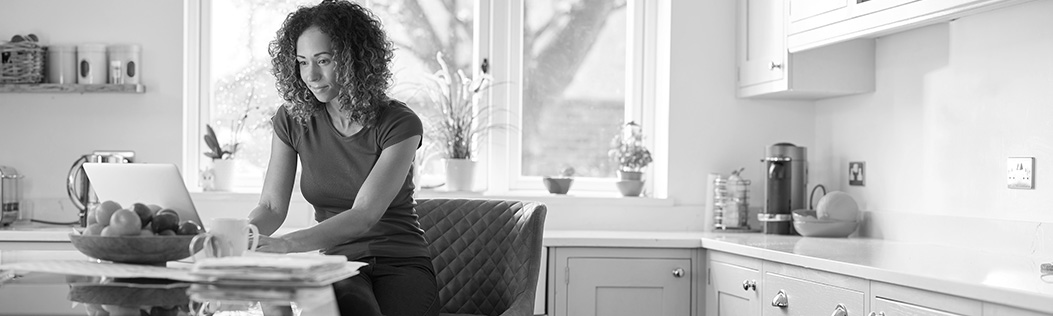 A woman sits in her kitchen and looks up her online benefits. 