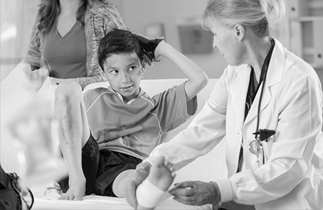 Photo of a young boy with a sprained ankle being seen by an emergency room doctor