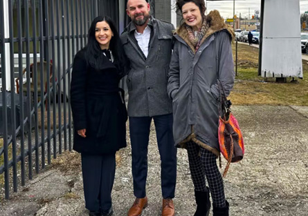 Three adults standing together outdorrs on a city sidewalk.